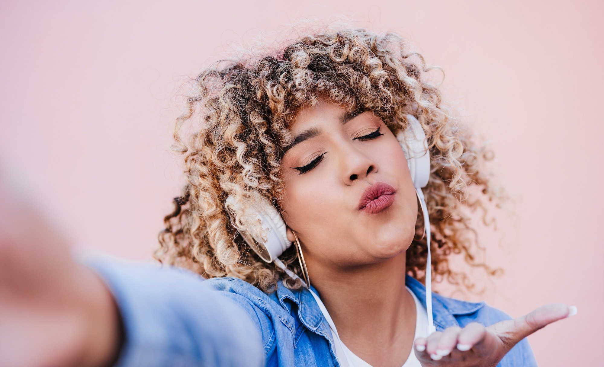 happy curvy hispanic woman with afro hair in city using mobile phone and headset. Body positivity
